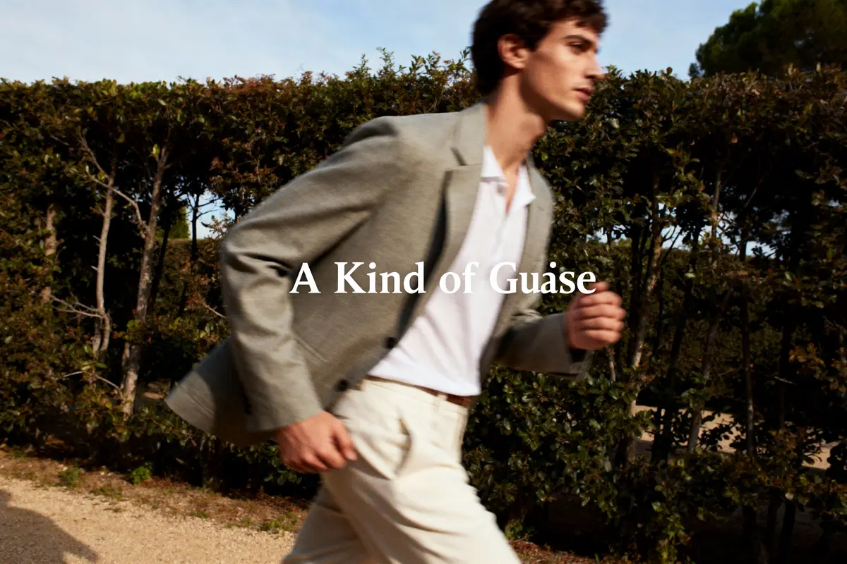 Homme en mouvement portant costume beige, chemise blanche, texte "A Kind of Guàse" en surimpression.