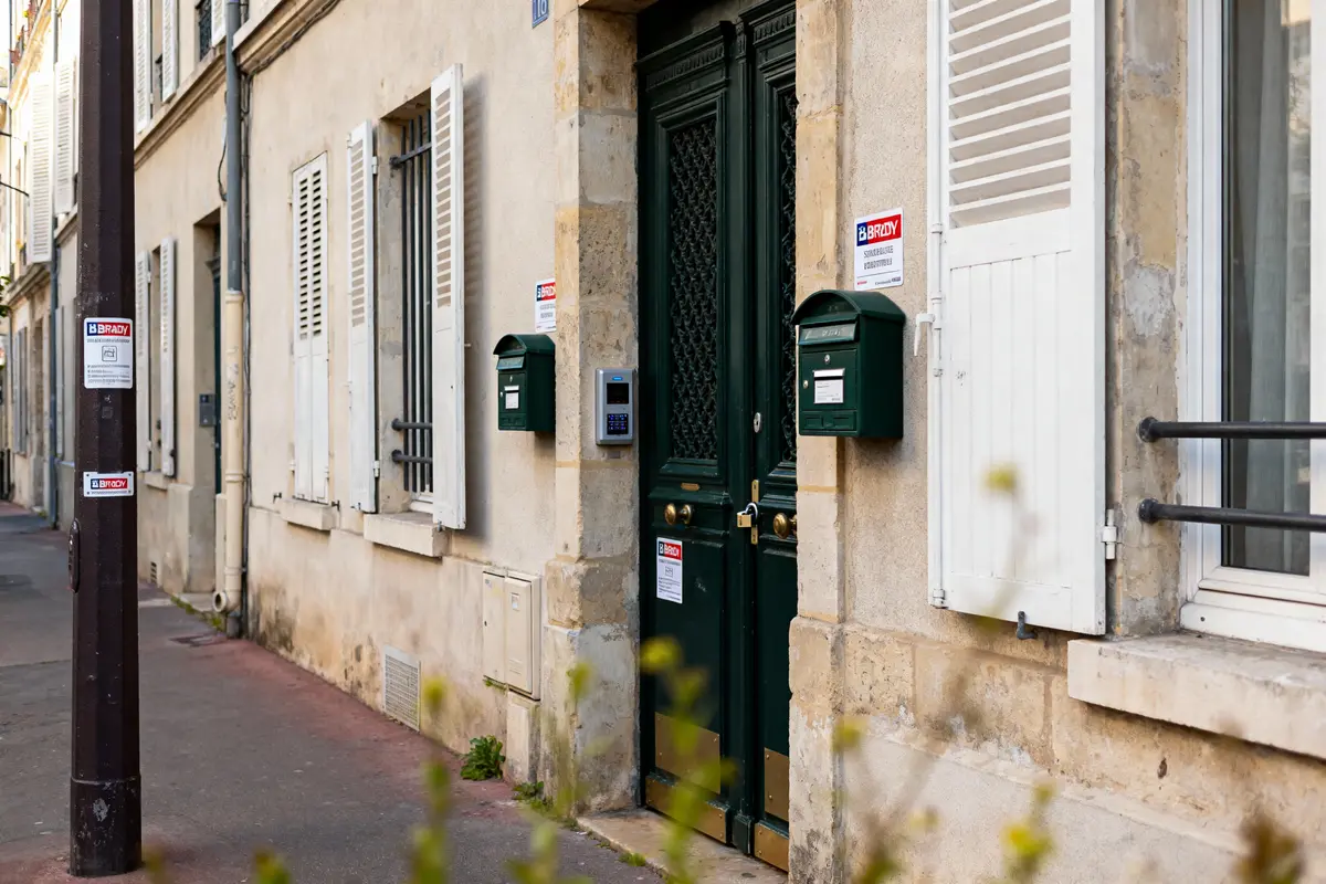 Façade de bâtiment urbain avec porte, boîte aux lettres verte et fenêtre. Rue pavée avec lampadaire.
