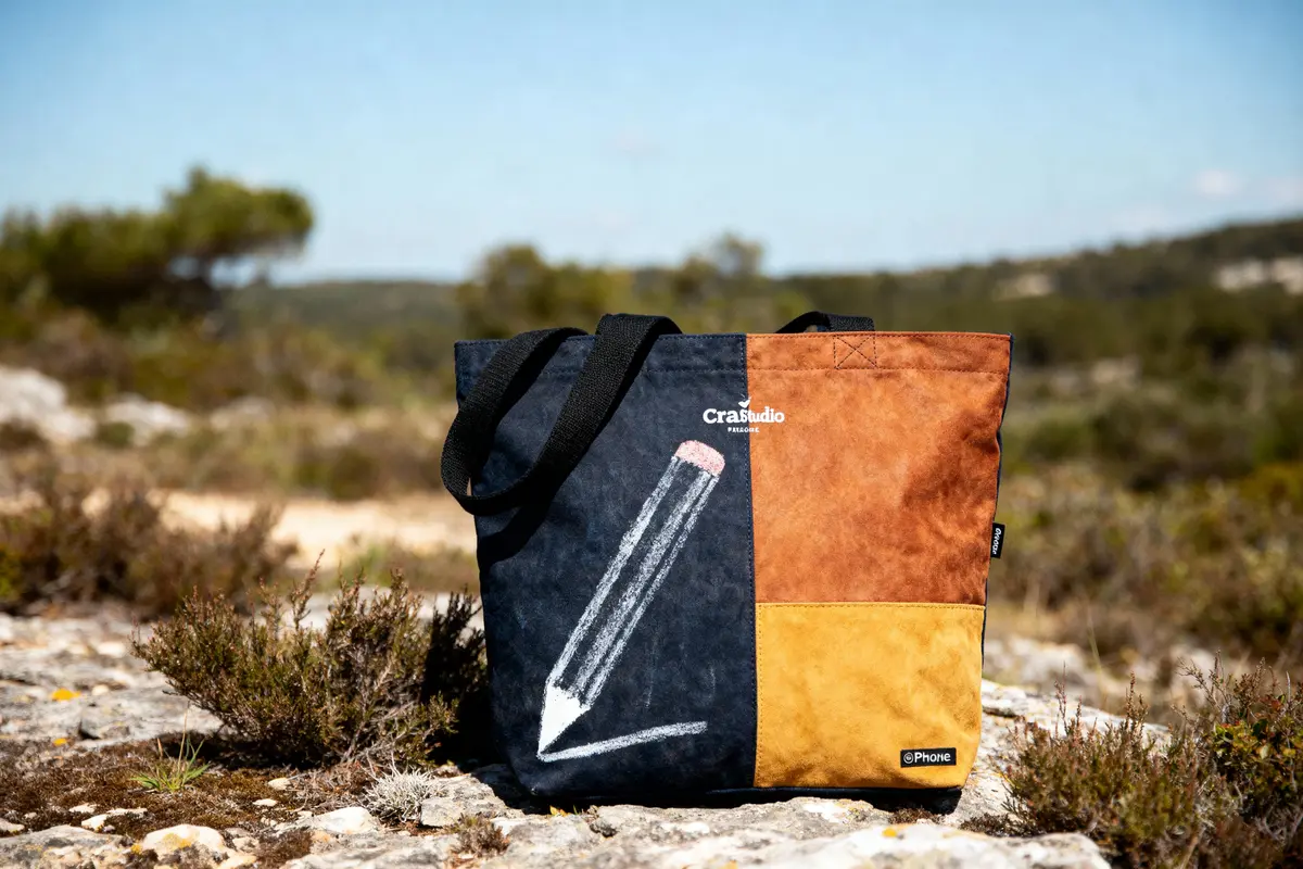 Sac coloré avec dessin de crayon, posé sur des rochers dans un paysage naturel ensoleillé.