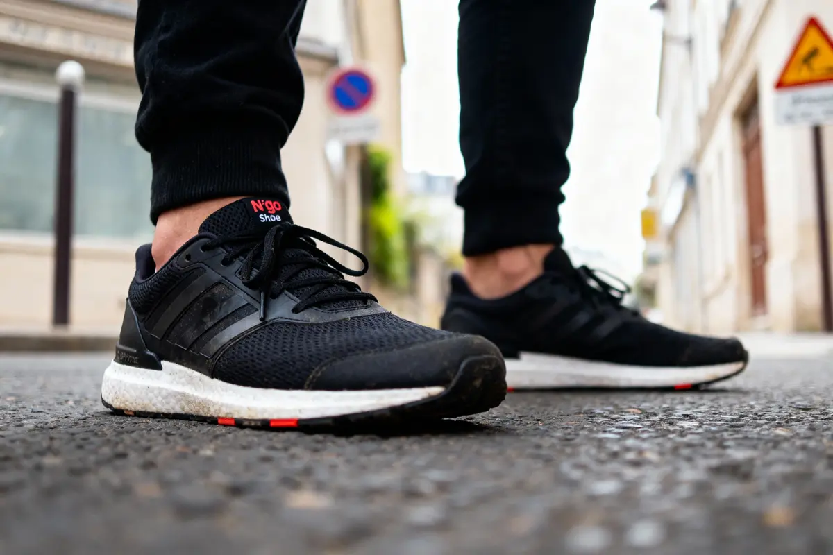 Deux pieds portant des baskets noires sur une rue pavée en ville.