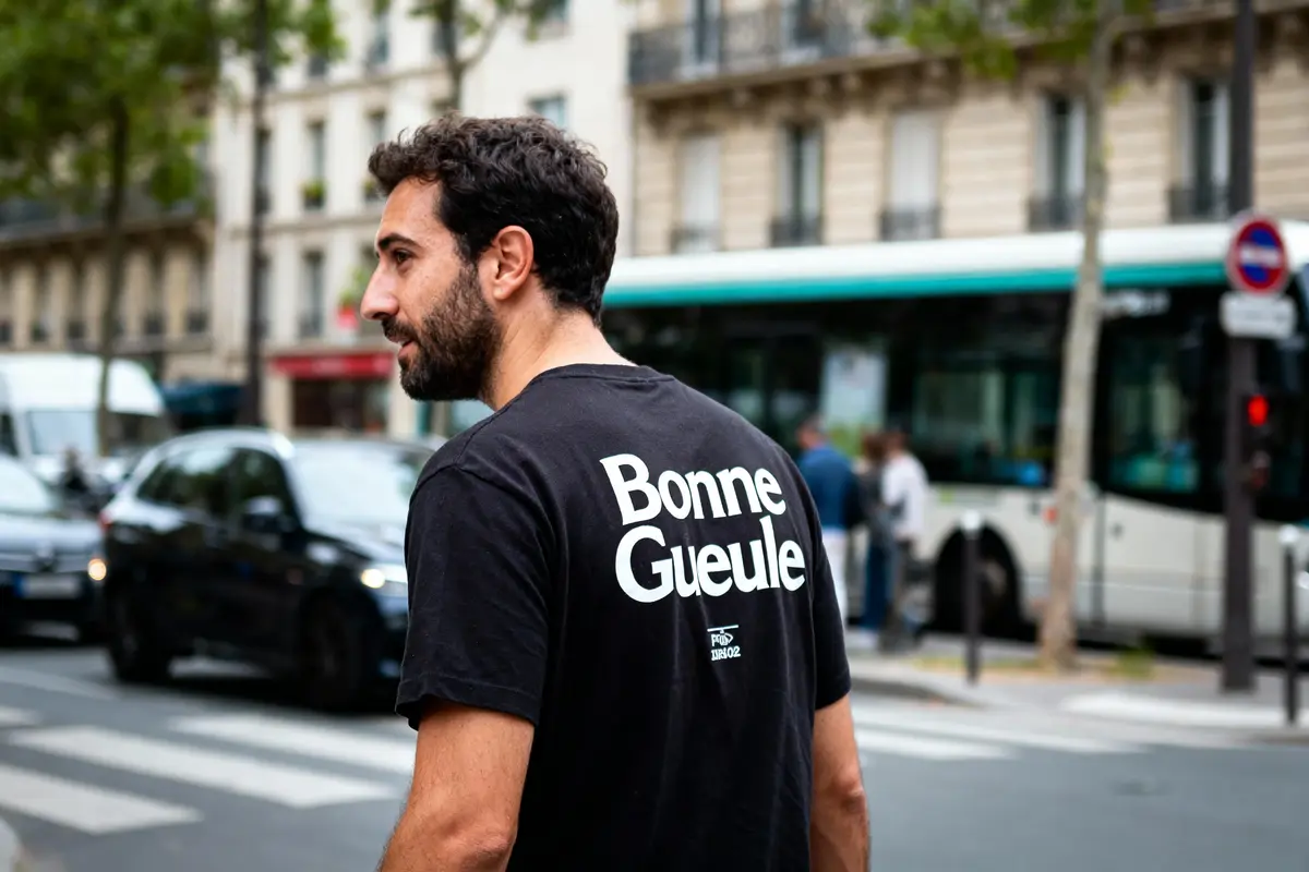 Homme portant un t-shirt "Bonne Gueule" dans une rue urbaine, voitures et bus en arrière-plan.