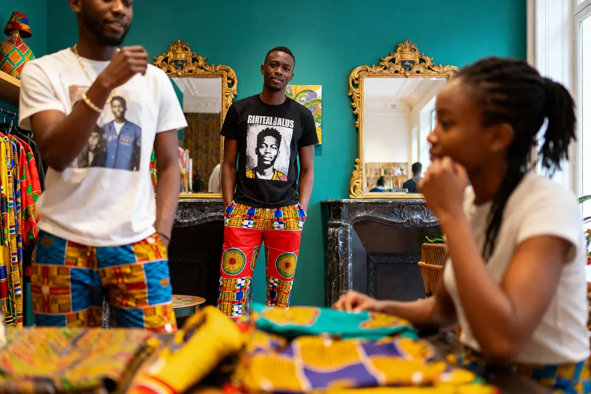 Trois personnes portant des vêtements colorés dans une boutique avec miroirs dorés et tissus africains.