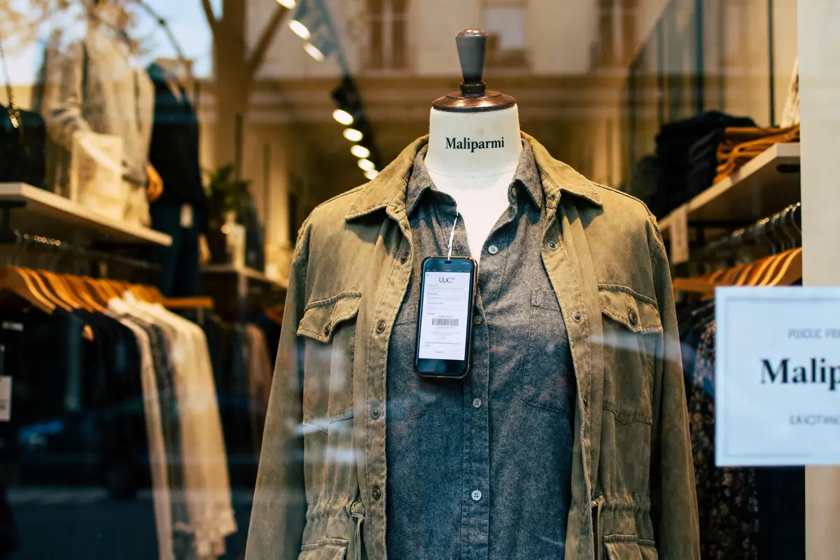 Mannequin en vitrine portant veste verte et chemise grise, avec étiquette attachée, magasin de vêtements.