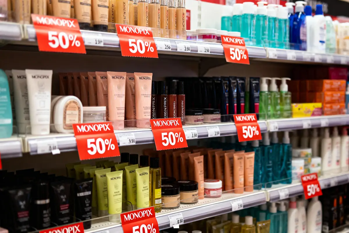 Rayons de produits cosmétiques avec étiquettes de réduction "50%" en supermarché, divers emballages colorés visibles.