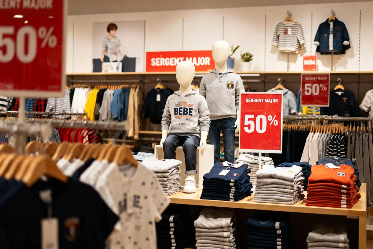 Magasin de vêtements pour enfants Sergent Major avec soldes de 50 %, mannequins et vêtements sur tables et cintres.