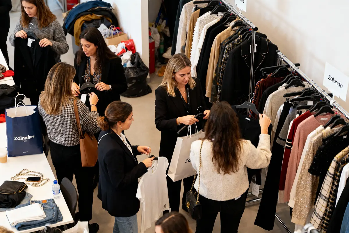 Femmes faisant du shopping dans un magasin de vĂŞtements, portant des articles sur cintres, autour d'une table, sacs Zalando.