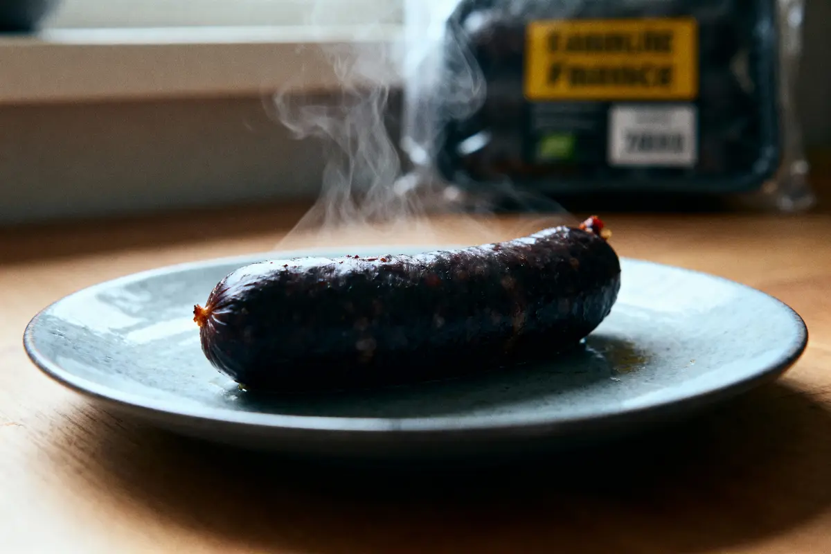 Saucisse fumante sur assiette grise, emballage en arrière-plan, éclairage naturel sur table en bois.