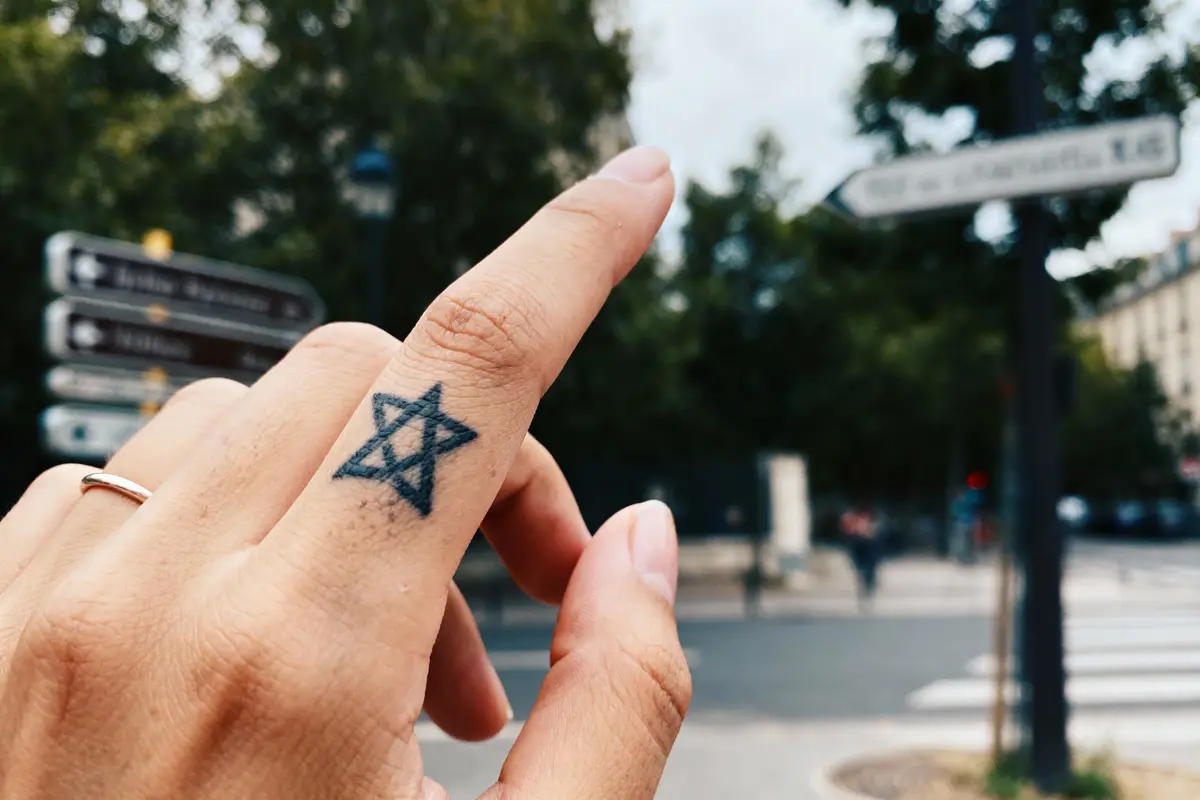 Doigt avec tatouage étoile de David, fond urbain flou avec panneaux.