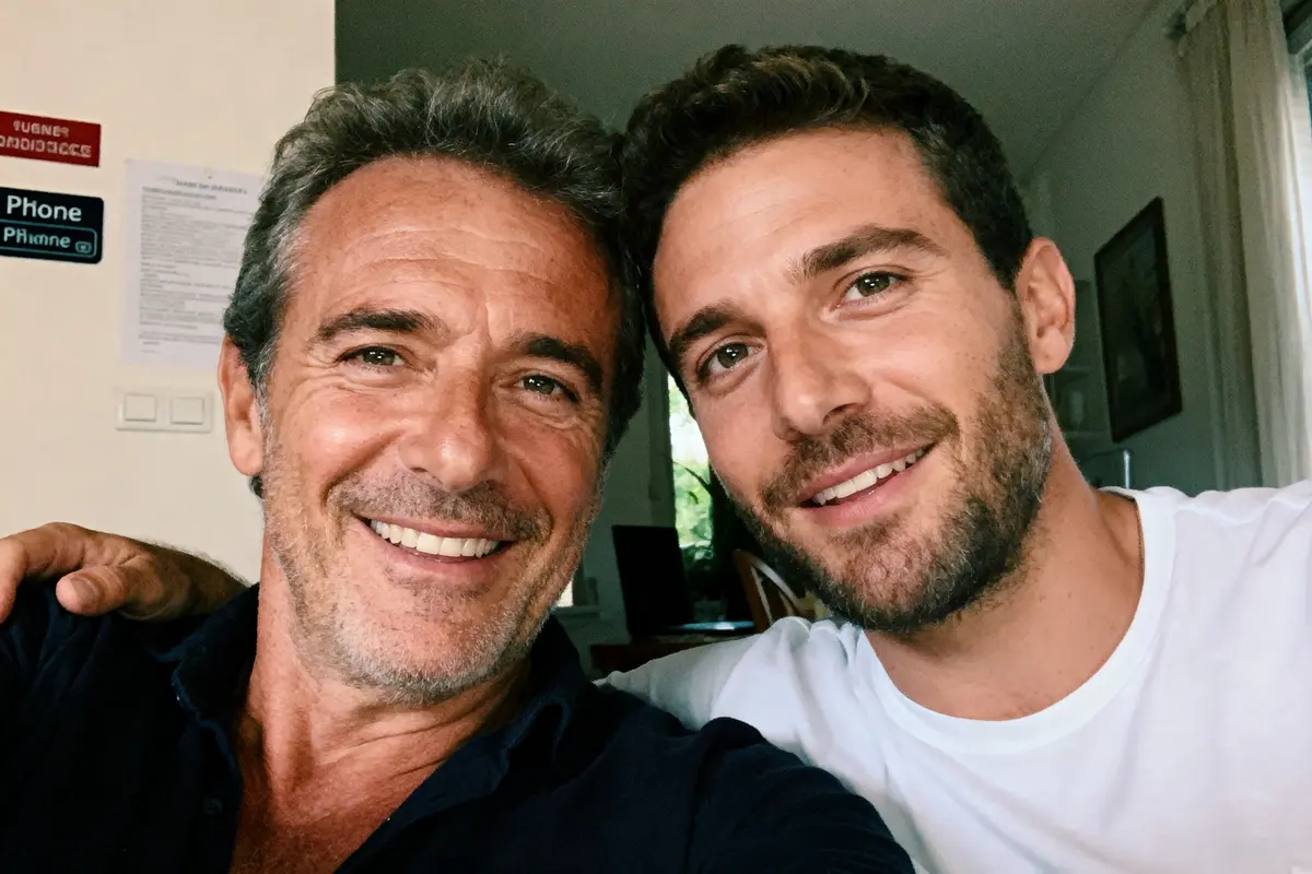 Deux hommes souriants prennent un selfie ensemble à l'intérieur, ambiance chaleureuse et conviviale.
