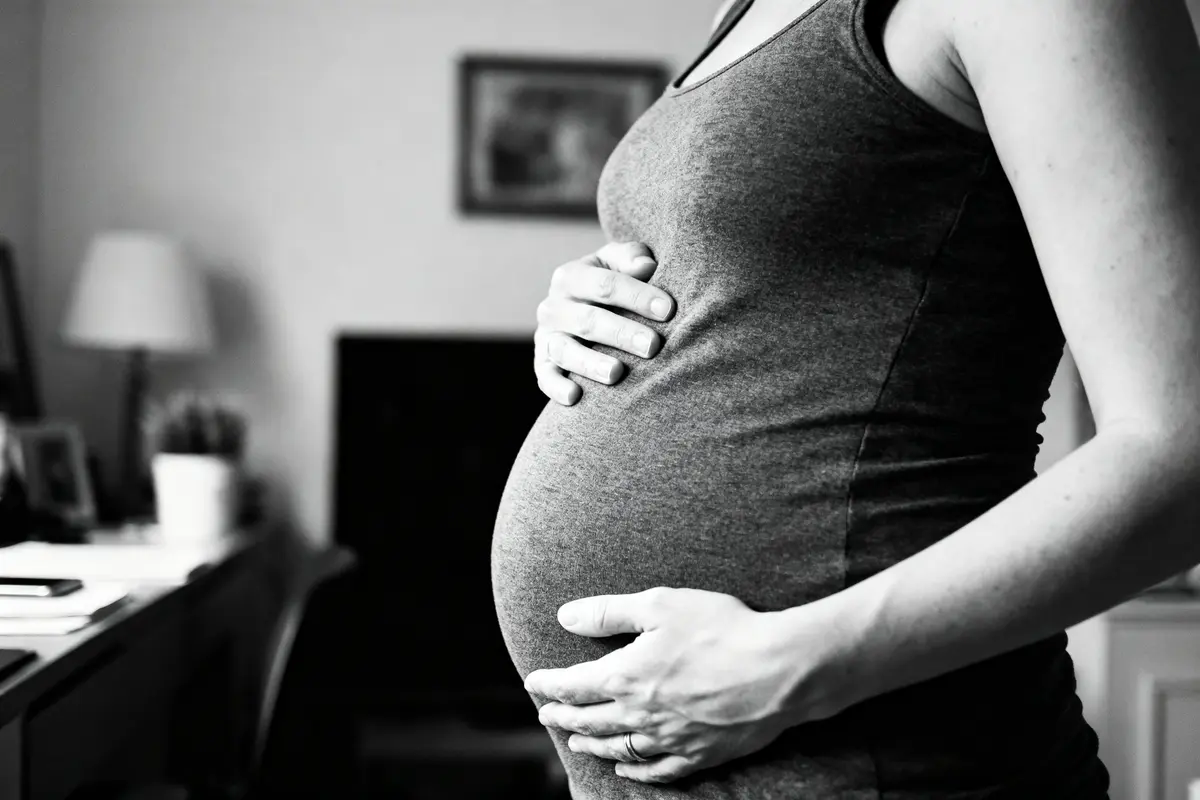 Femme enceinte tenant son ventre, photographie en noir et blanc à l'intérieur d'une maison.