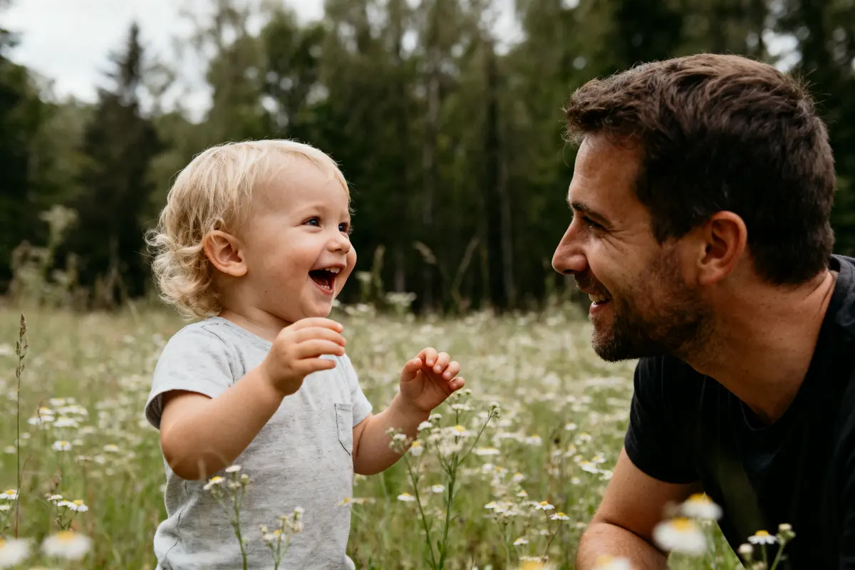 Un enfant et un homme sourient ensemble dans un champ fleuri, entourés de verdure.