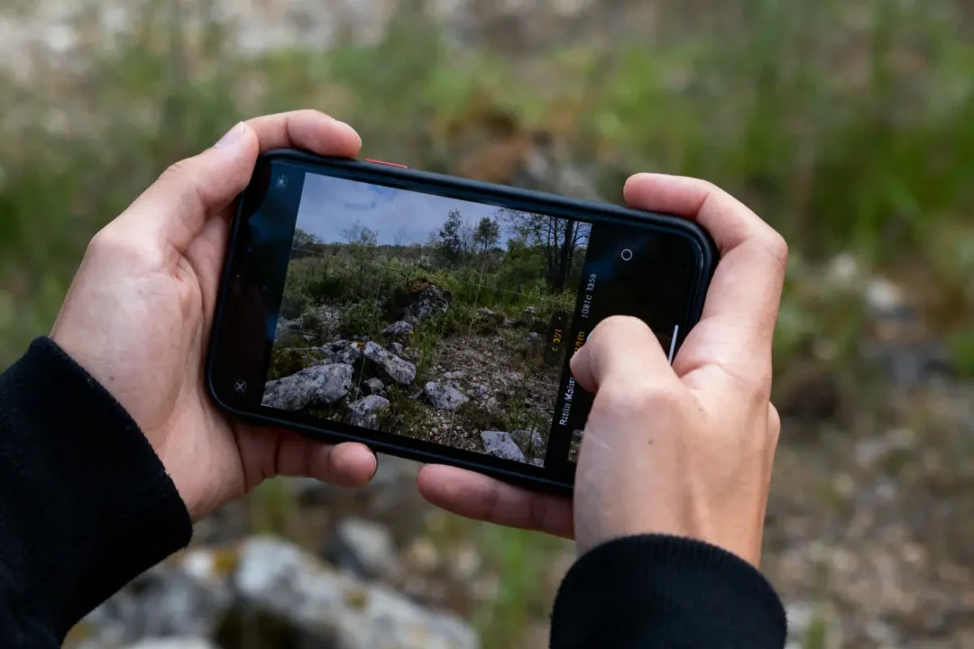 Personne prenant une photo d'un paysage naturel à l'aide d'un smartphone, avec des rochers et végétation visible.
