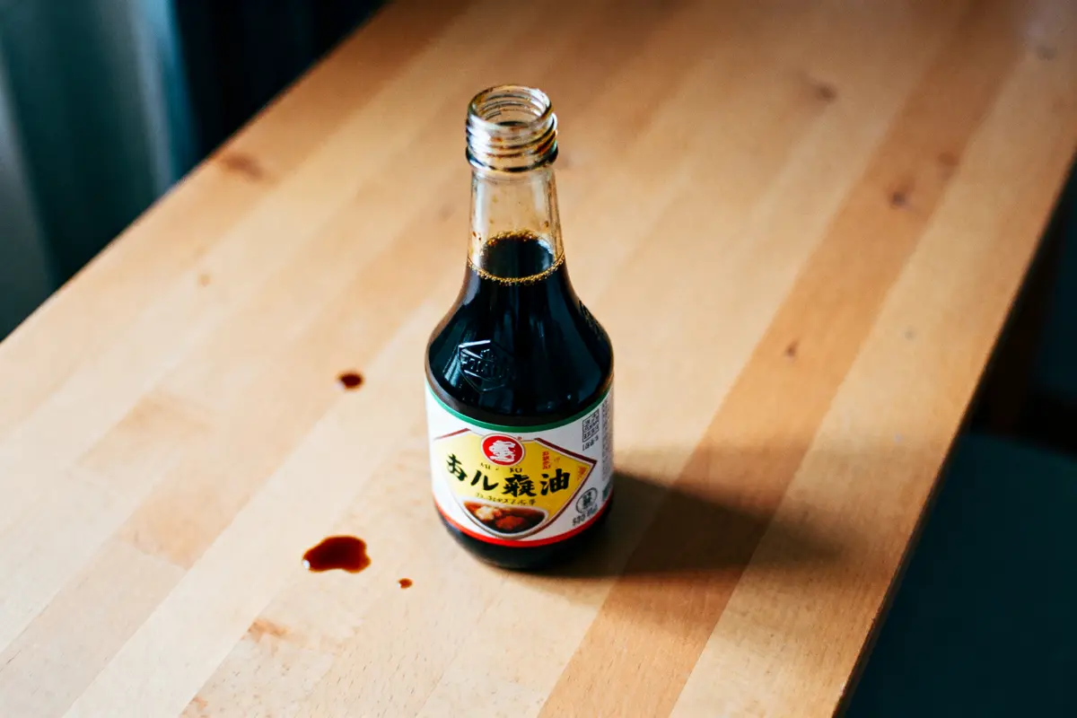 Bouteille de sauce soja ouverte sur table en bois, avec éclaboussures.