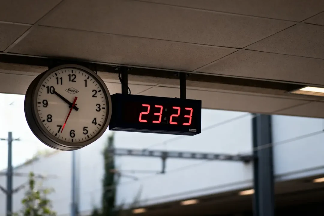 Horloge analogique et montre numérique affichant 23:23 dans une station de transport moderne.