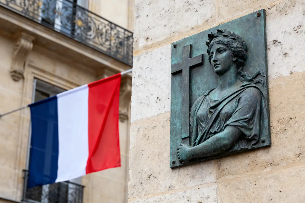 Plaque représentant une femme avec croix, drapeau français en arrière-plan, façade de bâtiment en pierre.