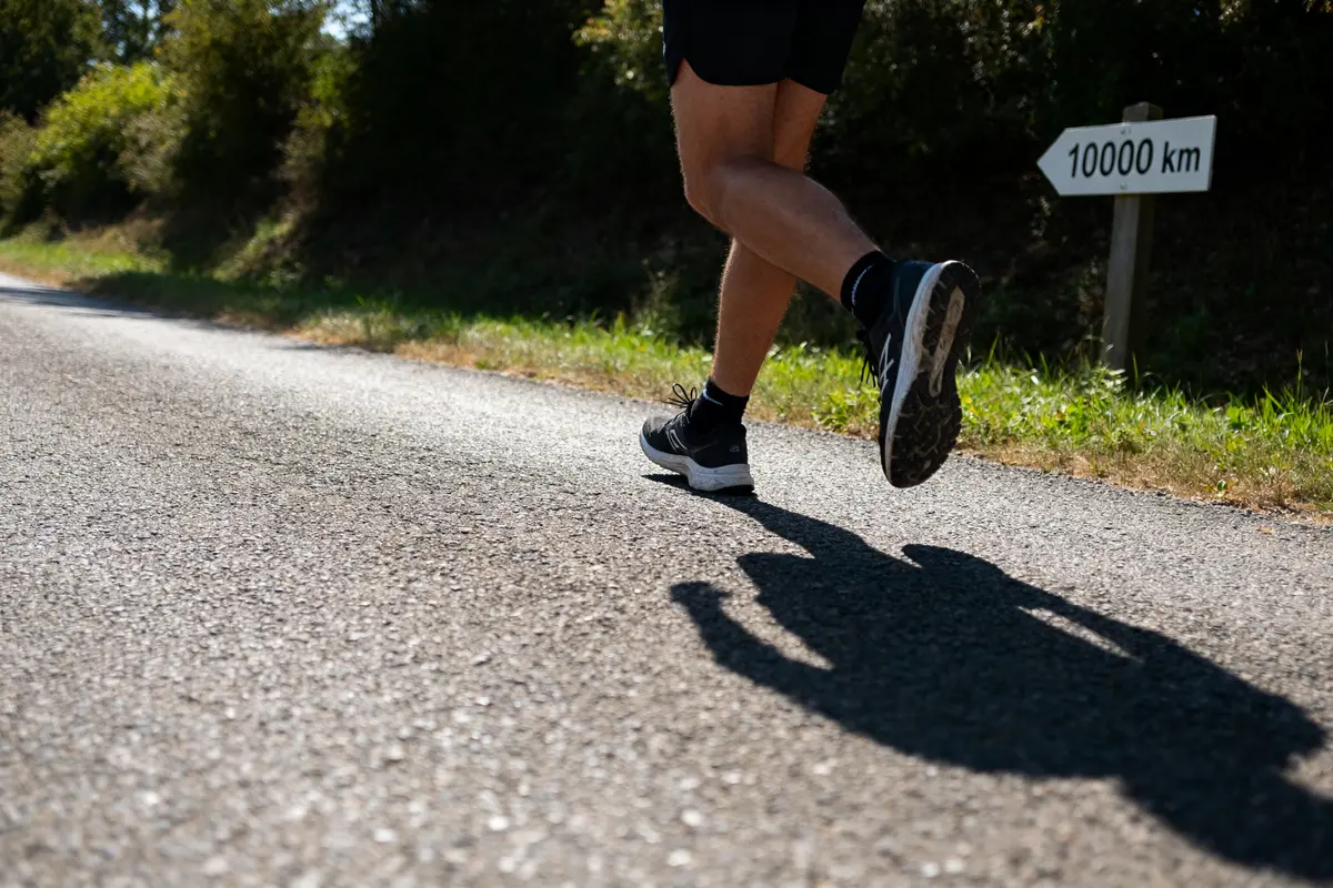 Coureur sur route ombragée avec panneau indiquant 10000 pas en kilomètres