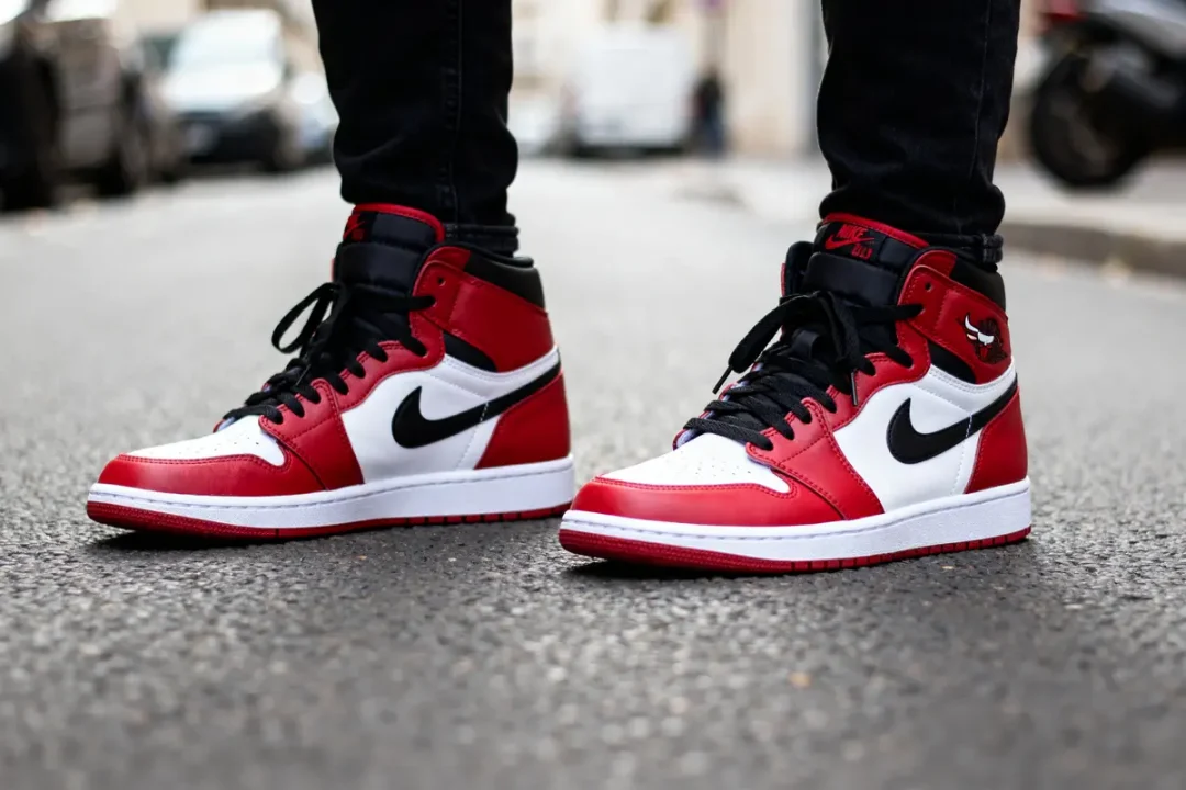 Personne portant des baskets Jordan 1 High rouges et blanches sur le trottoir urbain