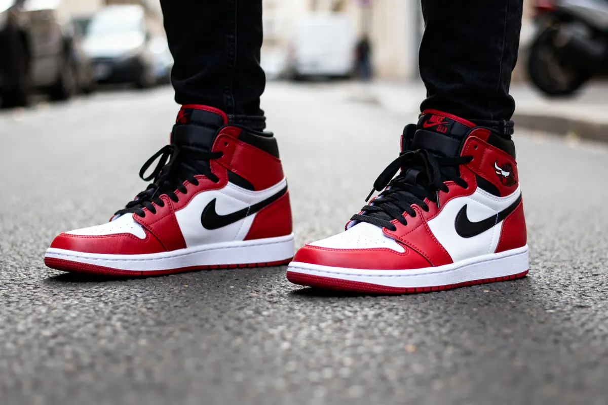 Personne portant des baskets Jordan 1 High rouges et blanches sur le trottoir urbain