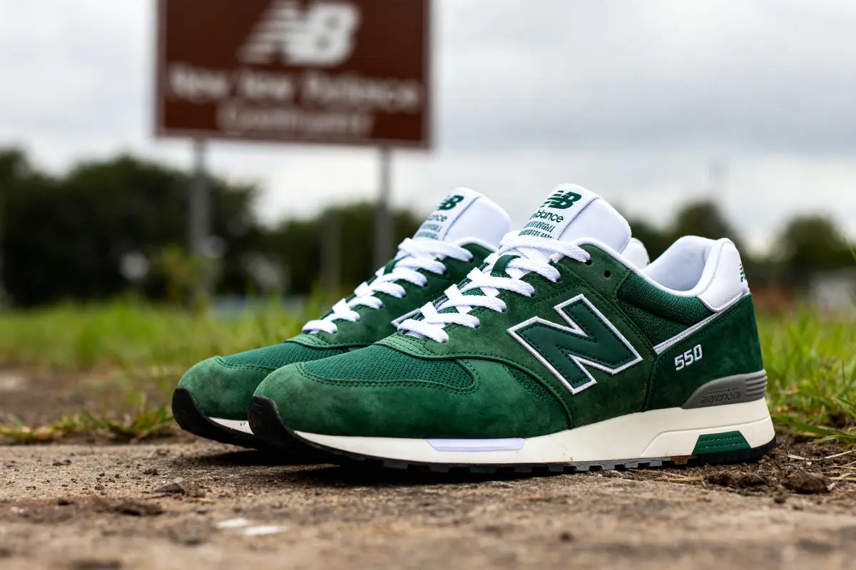 Chaussures vertes New Balance 550 green posées sur le sol extérieur devant une enseigne
