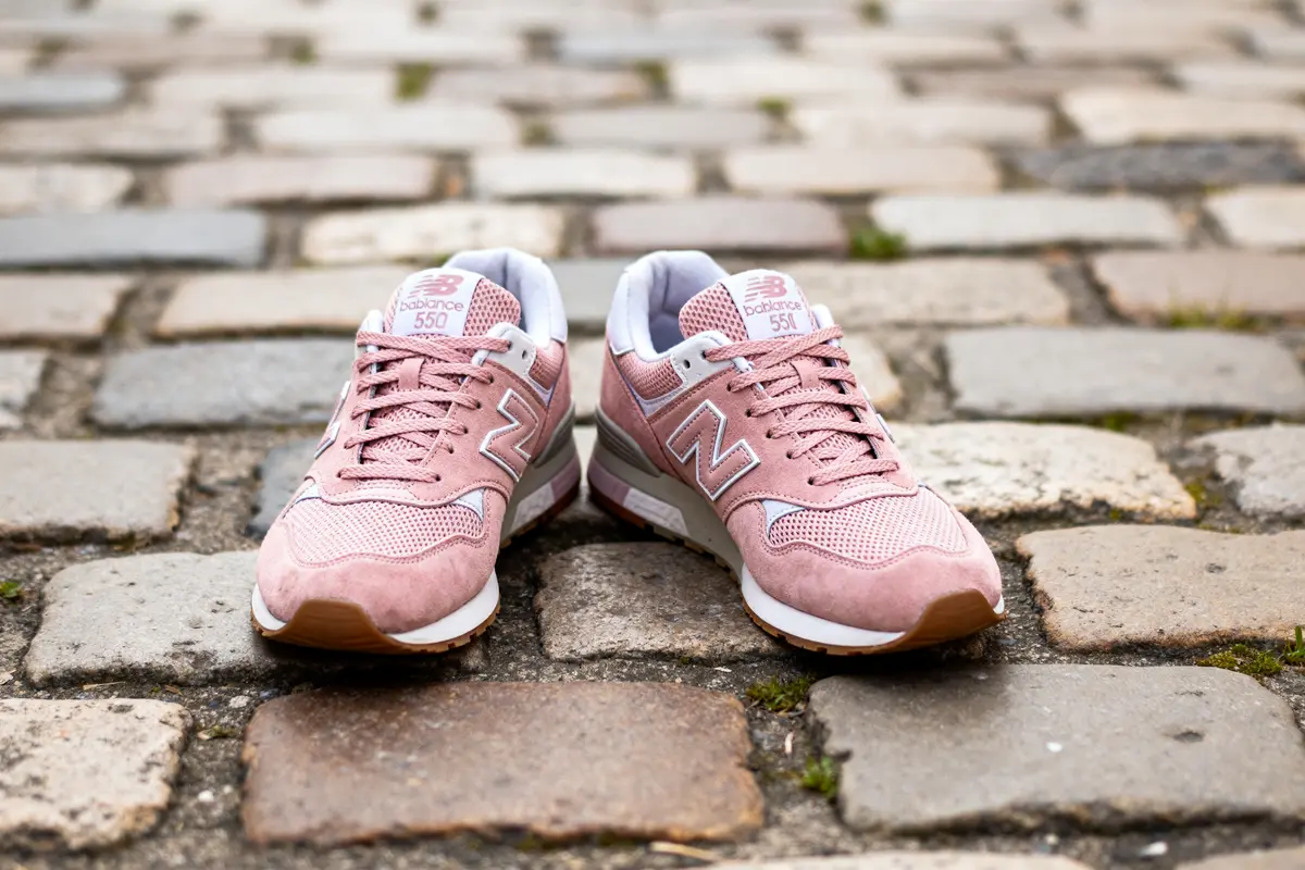 Chaussures New Balance 550 rose posées sur pavés urbains en arrière-plan flou