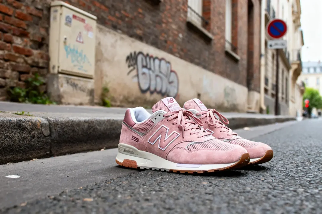 Chaussures New Balance 550 rose posées sur un trottoir urbain avec graffiti en arrière-plan