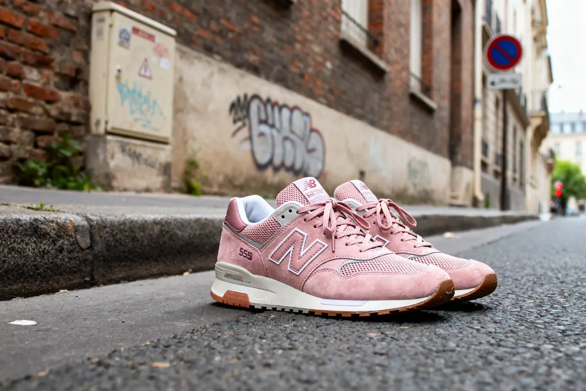 Chaussures New Balance 550 rose posées sur un trottoir urbain avec graffiti en arrière-plan