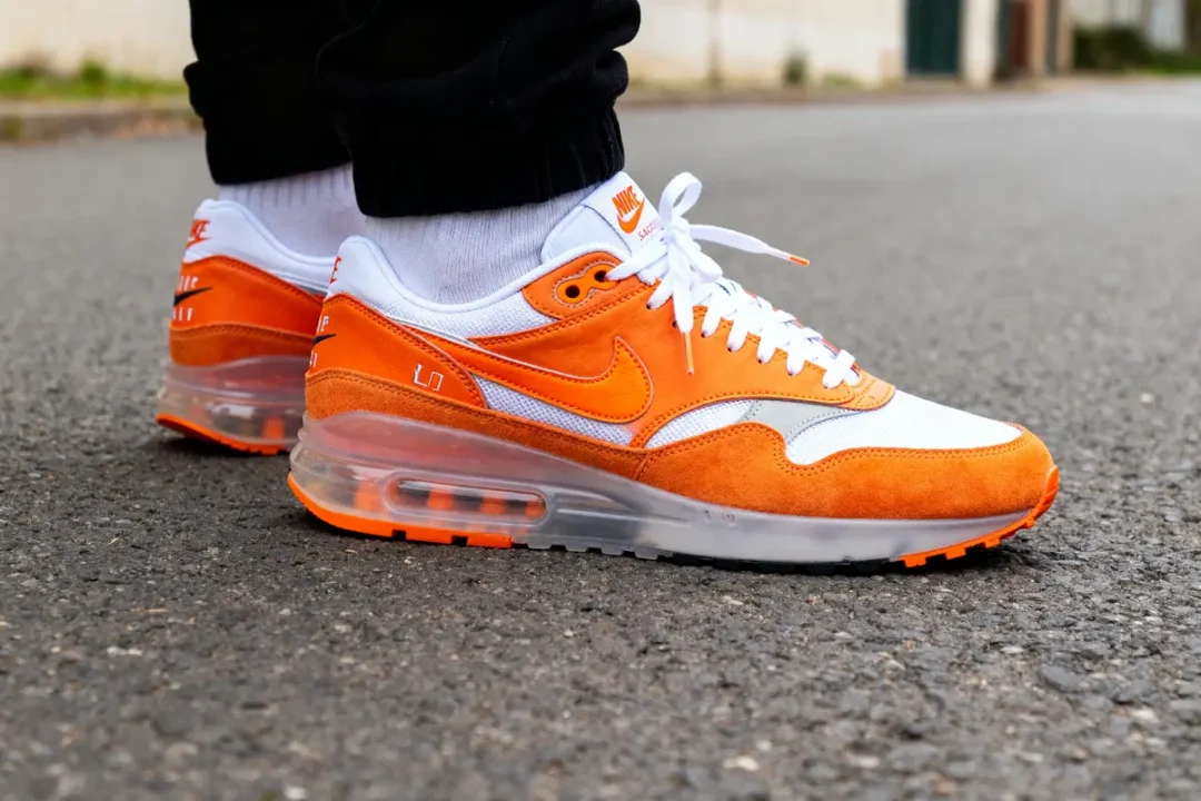 Baskets blanches et orange sur route grise, collaboration avec Sacai Orange visible