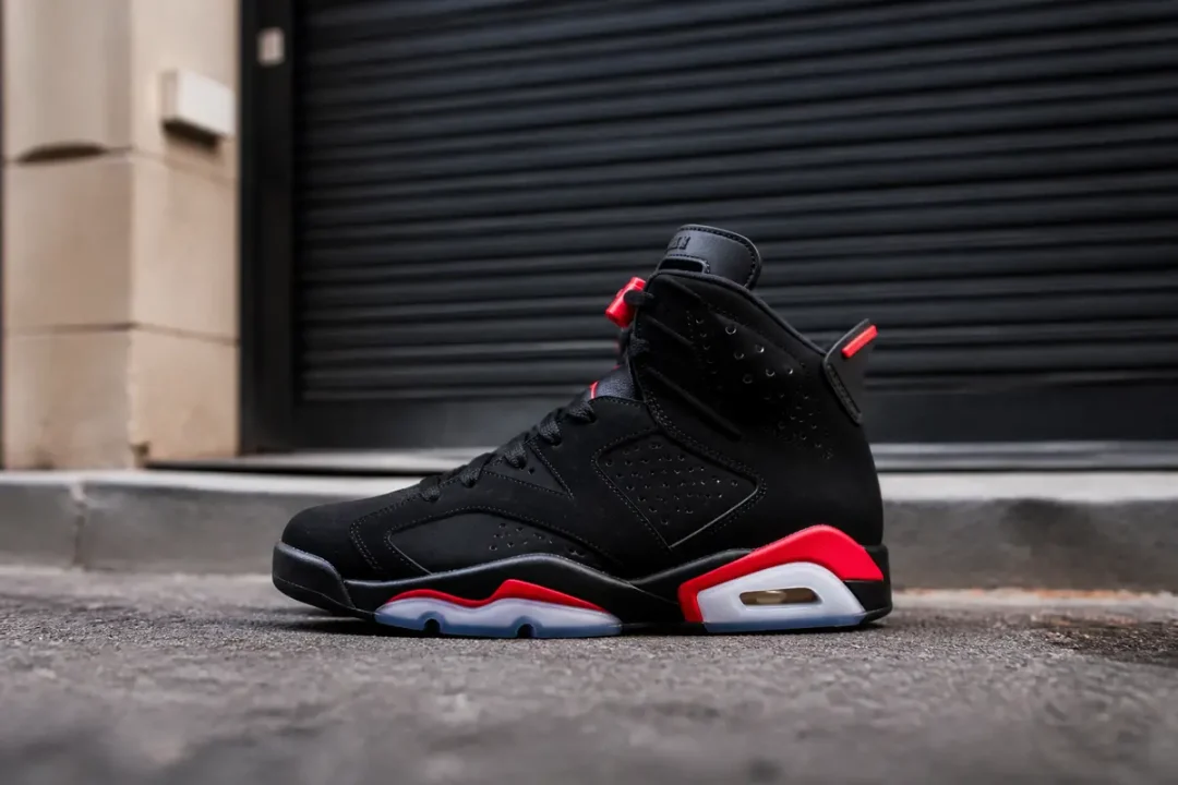 Chaussure noire et rouge Air Jordan 6 posée sur une chaussée devant porte fermée