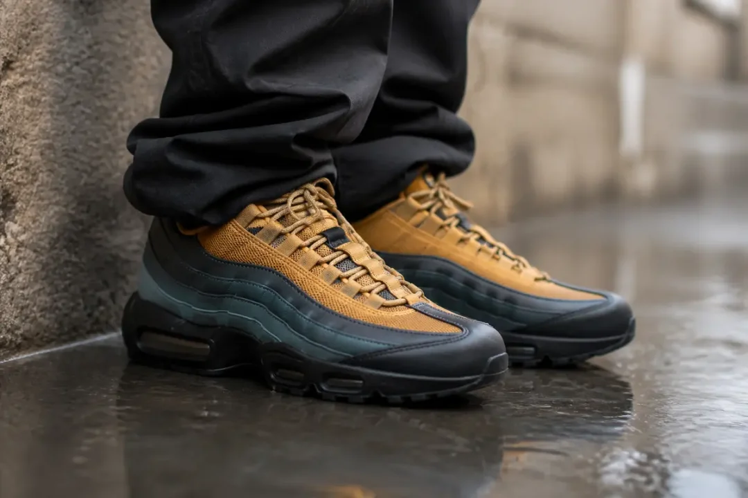 Personne portant des baskets Air Max 95 de Corteiz jaunes et noires sur sol mouillé