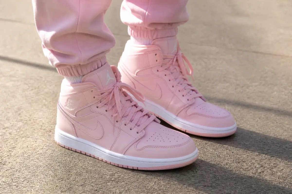Chaussures Jordan en rose pastel avec pantalon assorti sur fond gris clair.