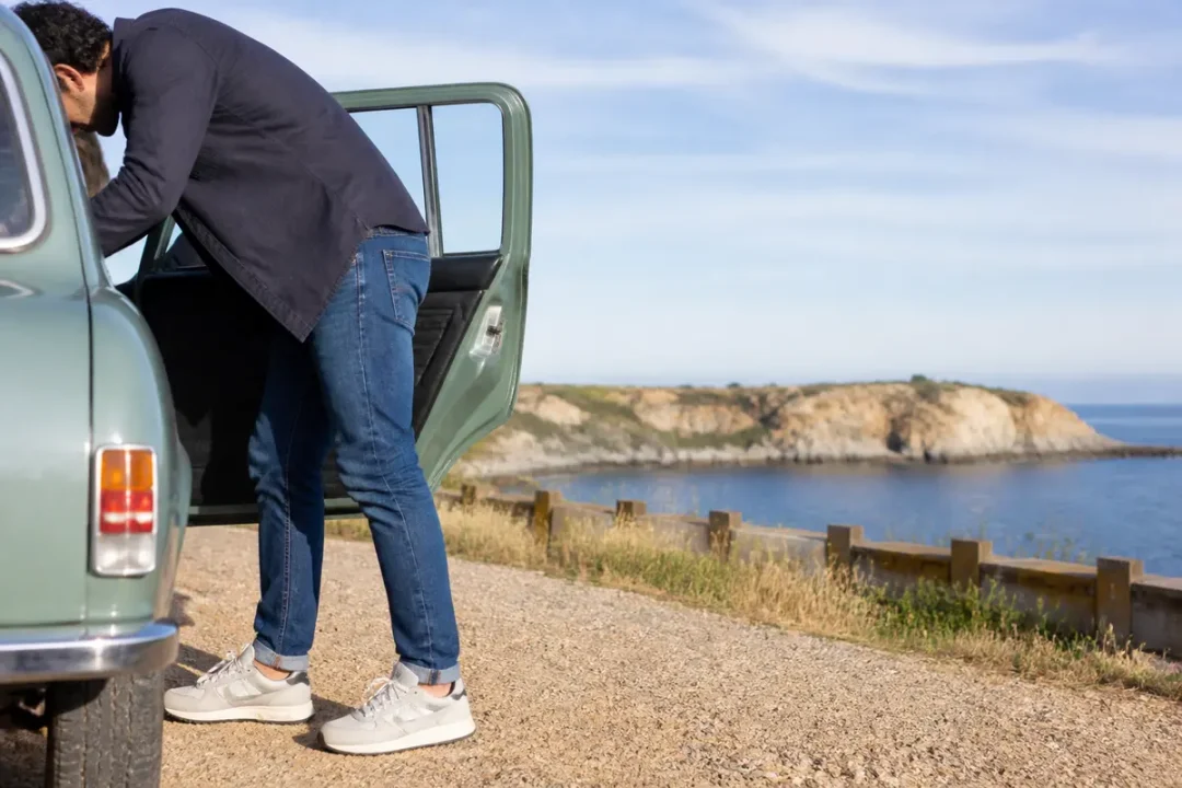 Homme debout près d'une voiture, portant des baskets avec un jean au bord d'une falaise